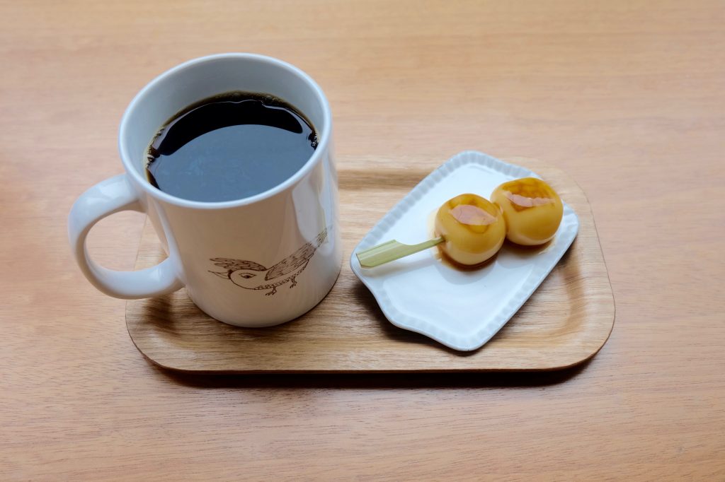 映画でも使用された珈琲「かわせみ」が入ったマグカップにはヨダちゃんのロゴが。お団子には、内藤さんが生み出したイラスト「半吉さん」も。